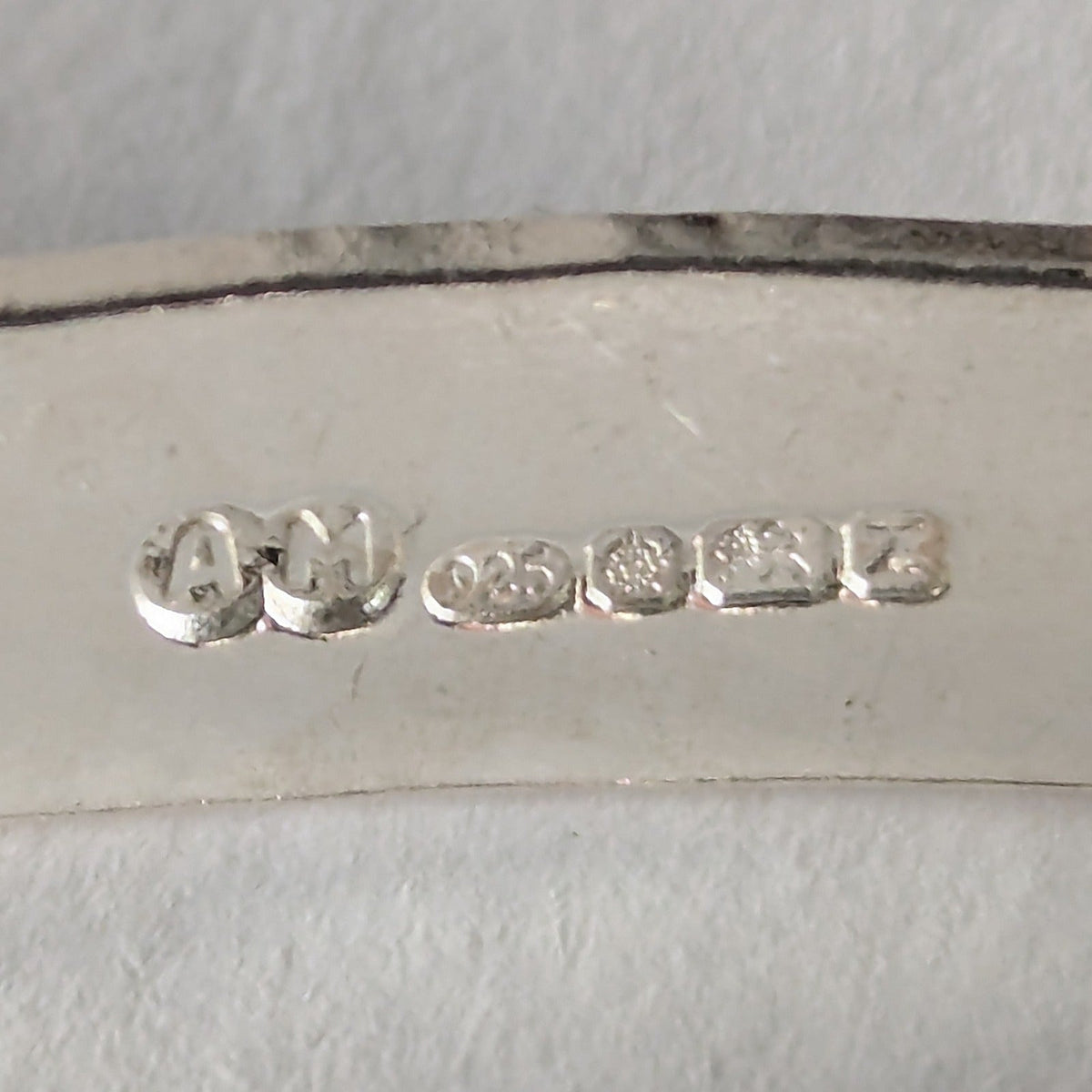 A full UK hallmark struck into the inside of a sterling silver bangle: Anna's AM maker's mark, 925, the Sheffield rose, the lion passant and the date letter