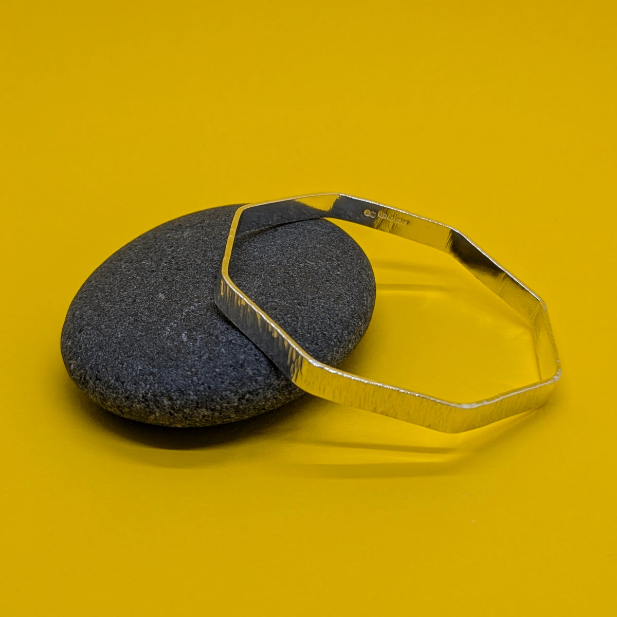 Hallmarked sterling silver octagonal textured bangle resting on a grey pebble